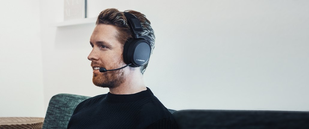 
 A user smiling while wearing the Arctis Pro Wireless, microphone in the extended position.
 