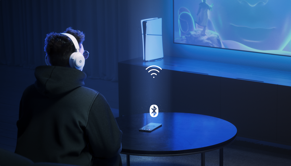 Rear view of a person sitting in light blue themed color room, focused on big screen with mobile on the table and PlayStation console next to tv, which implies multiple connection with all devices.