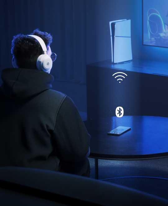 Rear view of a person sitting in light blue themed color room, focused on big screen with mobile on the table and playStation console next to tv, which implies multiple connection with all devices.